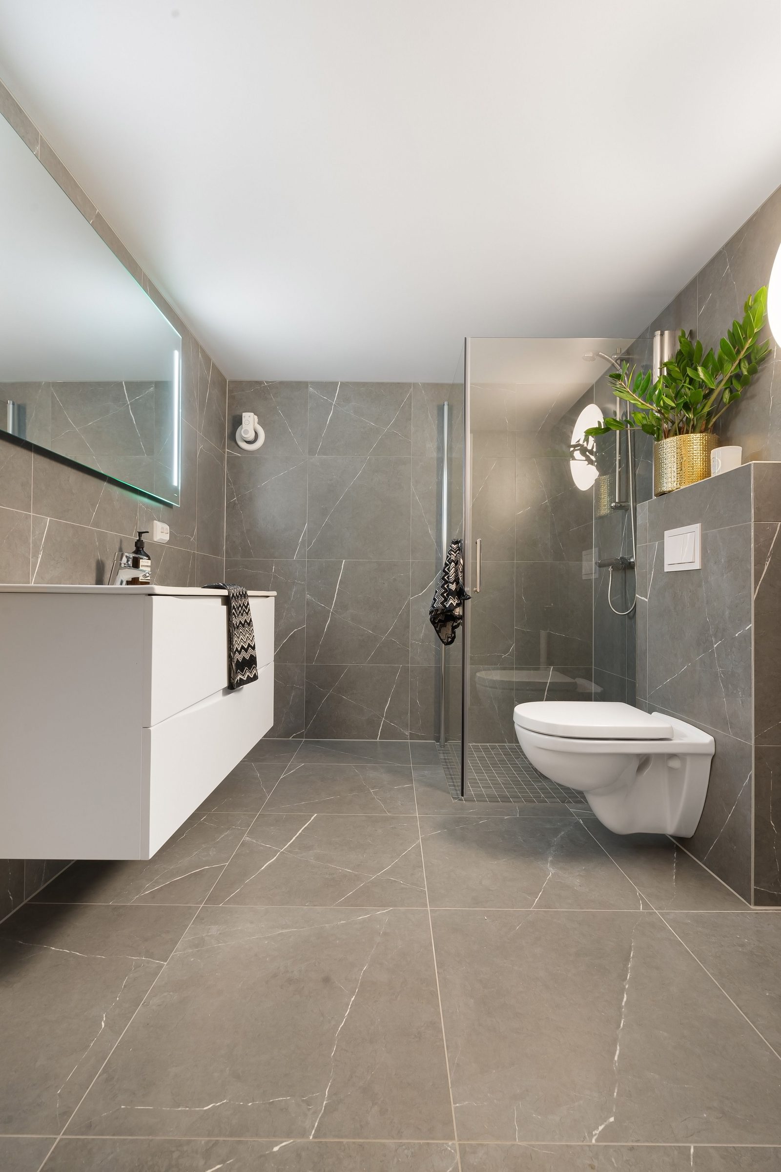 Modernisiertes Badezimmer mit grauen Fliesen und bodengleicher Dusche