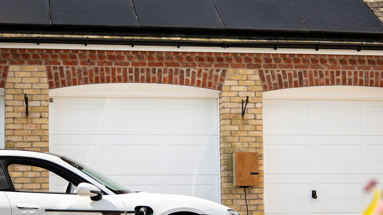 Garagendach mit Photovoltaikmodulen, Wallbox an der Backsteinwand und ladendes Elektroauto